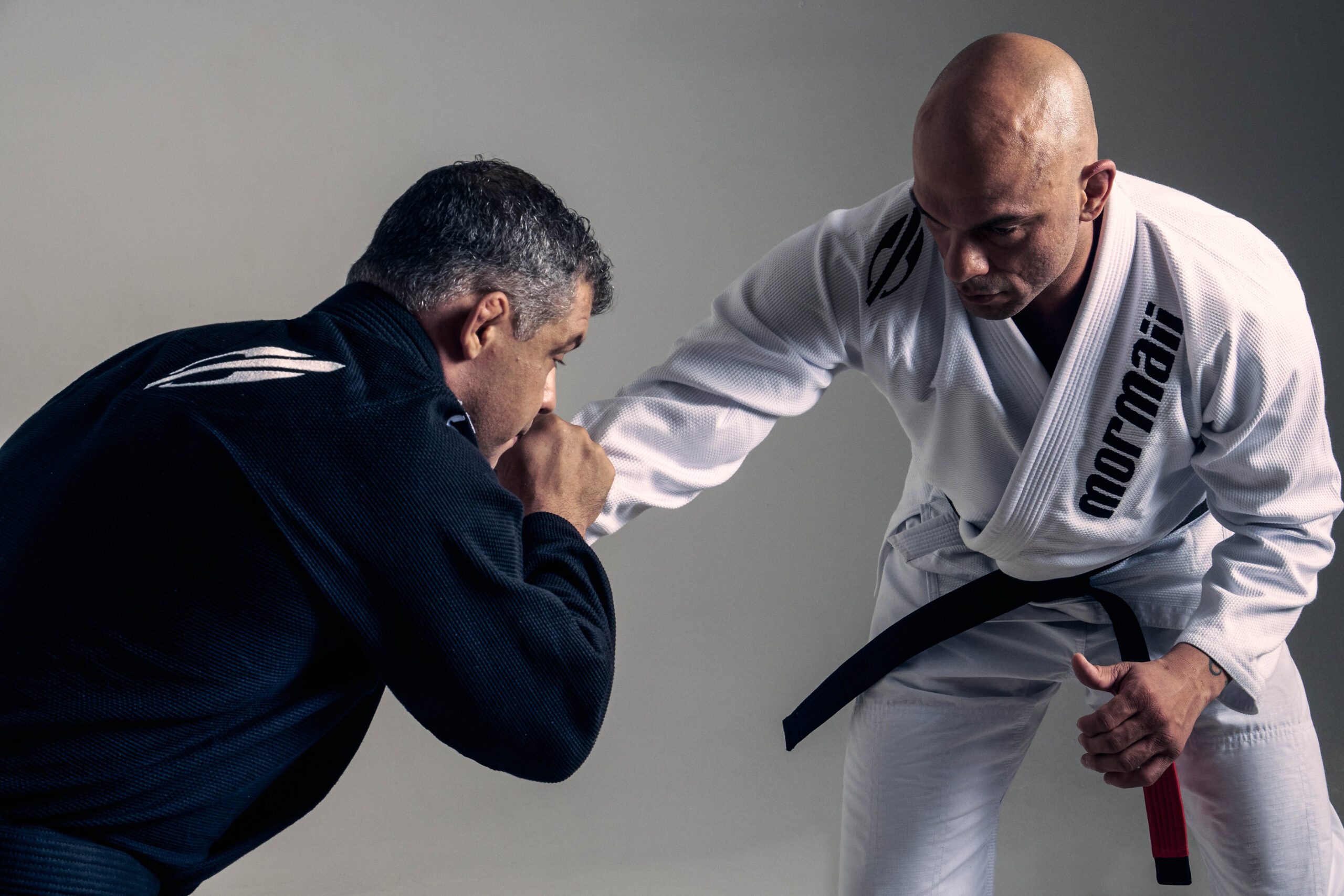 “Two athletes training Brazilian jiu-jitsu wearing Mormaii gis, one in black and one in white, during a grappling position on the mat.